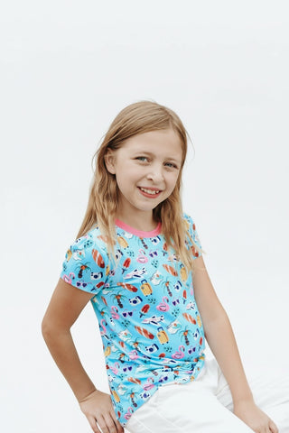 Young girl wearing a Twinflower Creations puff sleeve tee with a colorful tropical vacation print on a blue base.